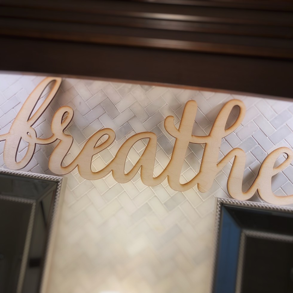 Wood cut sign that says "breathe" in script